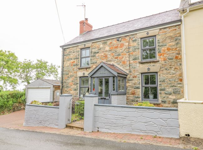 Stone house with gray framed windows and a gray porch with a gate and small brick driveway at Greenbanks in Dinas Cross Pembrokeshire
