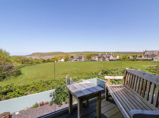 An outdoor area with a bench and table overlooking a field and houses at The Willows in Newport, Pembrokeshire
