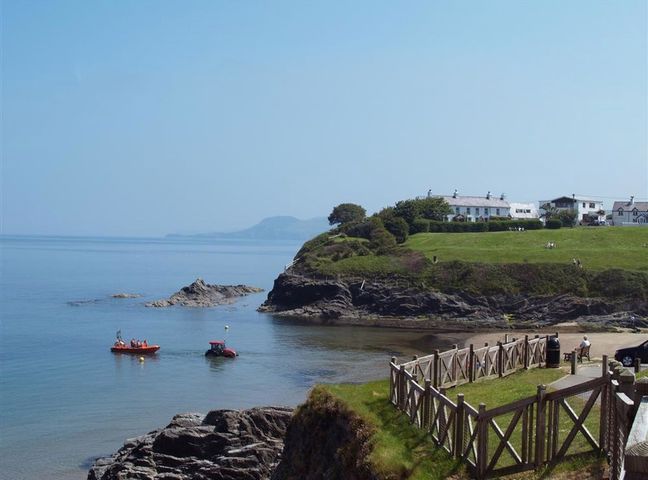 A coastal area with rocky shore a small boat a tractor and houses on grassy land at Beach Retreat in Aberporth