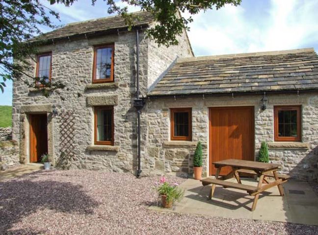 A stone house with wooden windows and doors with a wooden picnic table outside at Swallows Barn in Litton Slack near Cressbrook and Tideswell