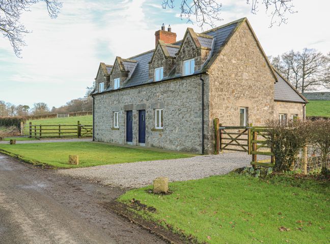 A stone house with blue doors and windows a gravel driveway and a wooden gate at Goose Cottage Caledon near Killylea
