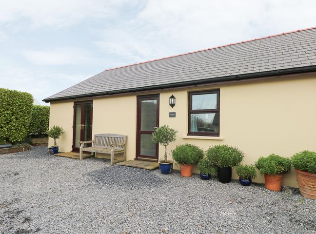 The exterior of a single-story building with a bench and several potted plants on a gravel area at Smugglers in Lydstep
