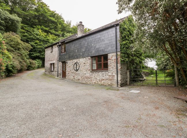 An exterior view of a stone house with slate cladding surrounded by trees and a metal gate at Ribby Barn in Lerryn