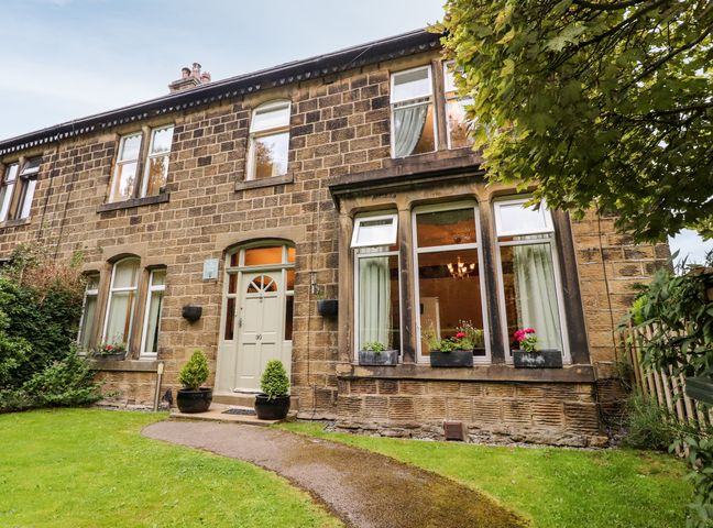 The front of a stone house with a pathway leading to a door and windows with flower boxes at The Thyme House in Haworth