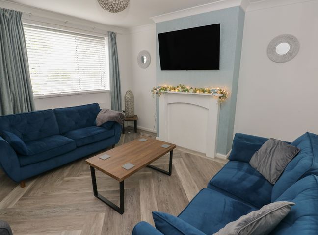 A living room with blue sofas and a coffee table at Cwtch Ar Y Mor in Burry Port