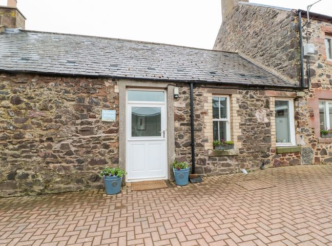 Exterior of a stone house with a white door and windows with flower pots on the ground at Adams House in Coldingham