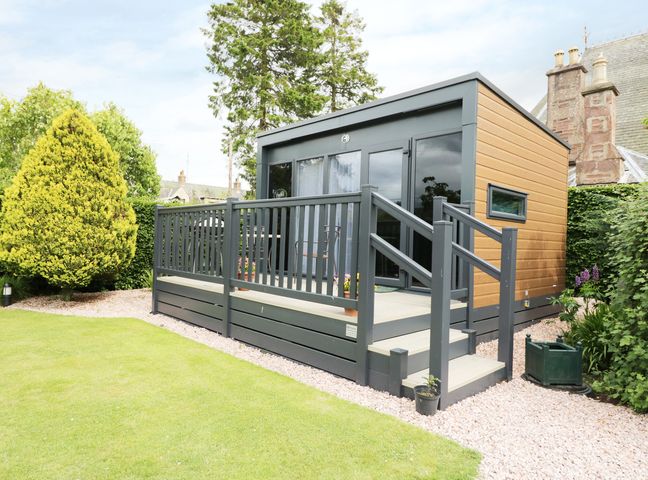 A small modern cabin with a wooden deck and railing in a garden with grass and trees at Cabin at the Tavern in Coupar Angus