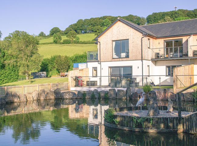 A modern house with wooden siding by a pond with rocks and bird statues at Defoe's View in Honiton