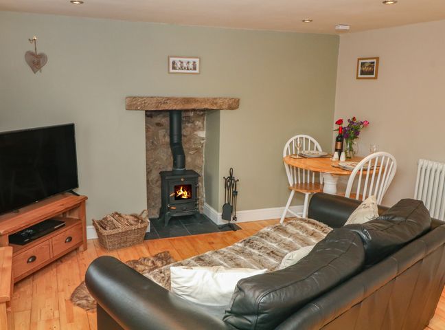 A living room with a wood burning stove basket of logs TV sofa and small dining table at The Snug in Middleton near Wirksworth