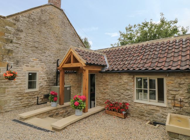 An exterior stone wall with a wooden porch and potted flowers on a gravel ground at The Coach House in Levisham