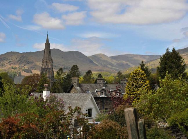 A village with houses and a church tower with mountains and trees in the background at Uldale in Ambleside