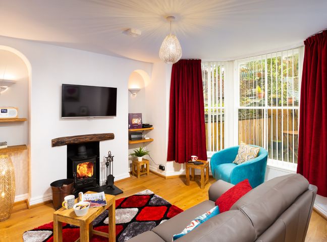 A living room with a wood burning stove a television and red curtains at Oak Cottage in Bowness
