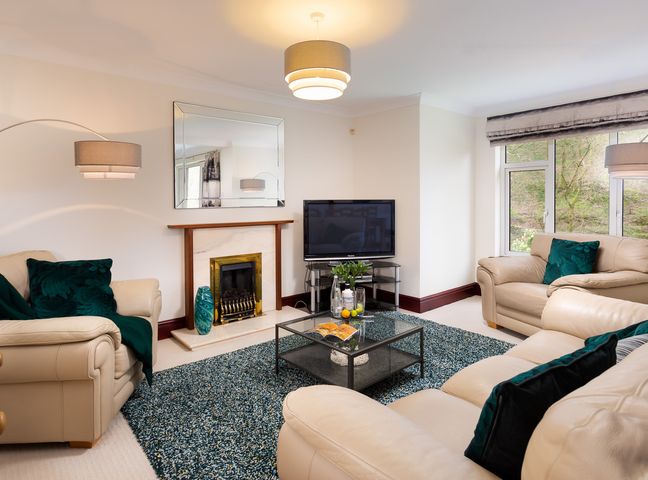 A living room with beige sofas green cushions a glass coffee table a fireplace and a television at Beech View in Ambleside