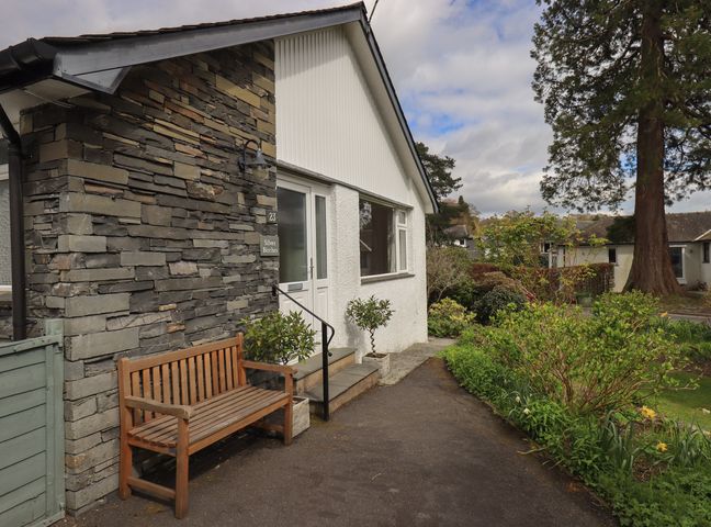 A pathway leading to a white house with a stone wall and wooden bench at Silver Birches in Windermere
