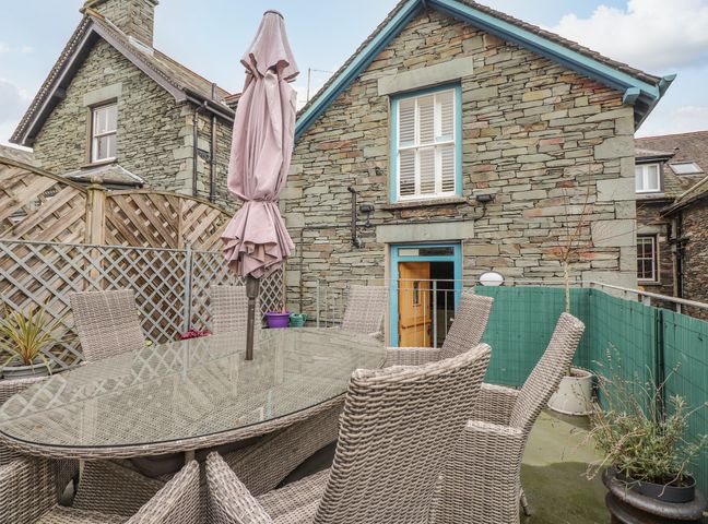An outdoor patio area with a glass table umbrella and wicker chairs next to a stone building at Rossett Holme in Ambleside
