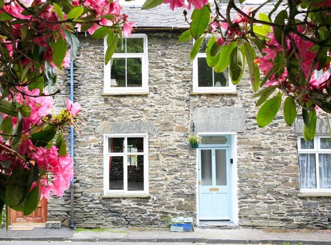 A stone house with white framed windows and a light blue door surrounded by pink flowers at Stone Cottage at Staveley in Staveley