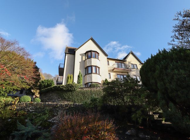 A multi-story building with balconies and bay windows surrounded by trees and bushes at Romney 14 in Ambleside