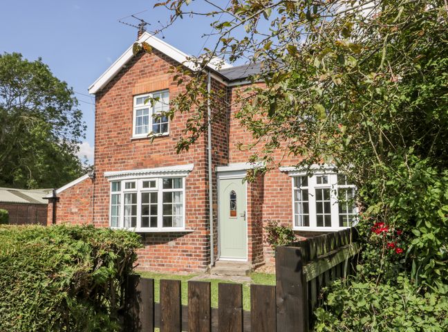A red brick house with white framed windows a green door and a wooden fence with bushes at Ryeby Garth in Skeffling near Patrington