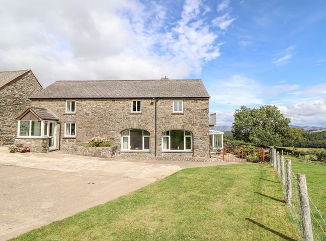 Stone house with windows and a small garden next to a fenced grassy area at The Stables At Cae Gwyn in Ruthin