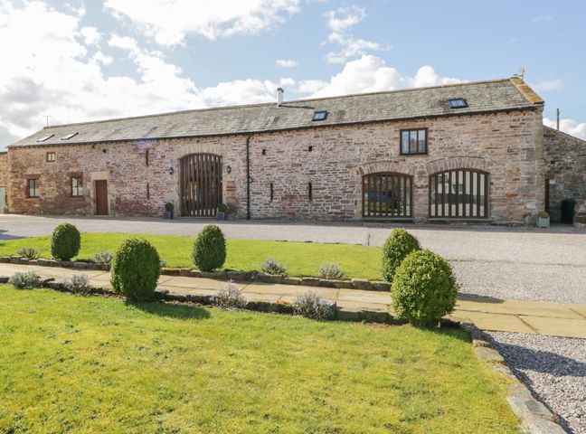 A stone barn building with arched windows and a driveway in front at Ashtree Barn in Great Asby near Appleby-In-Westmorland