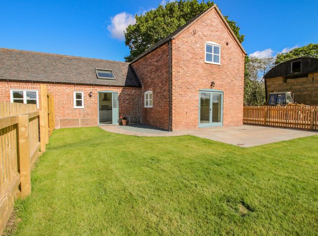 A brick house with blue doors and windows a fenced grassy yard and a tractor near hay bales at The Barn in Butlers Bank near Shawbury
