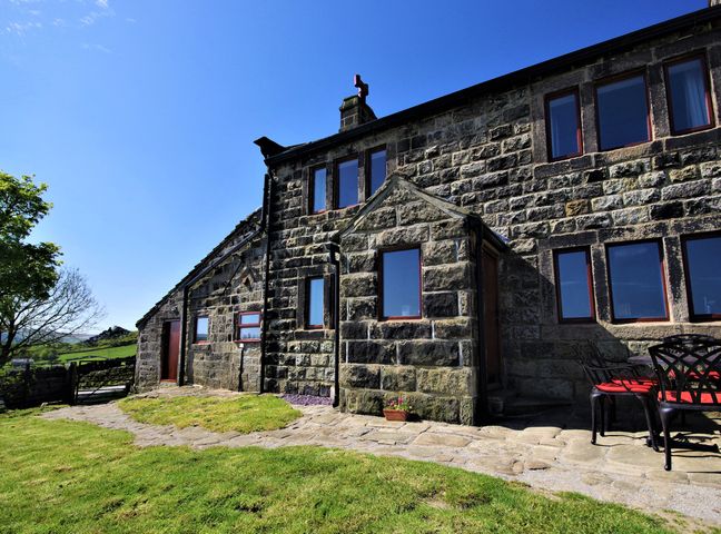 An exterior view of a stone building with multiple windows and an outdoor seating area at Rake Hey Farm in Todmorden