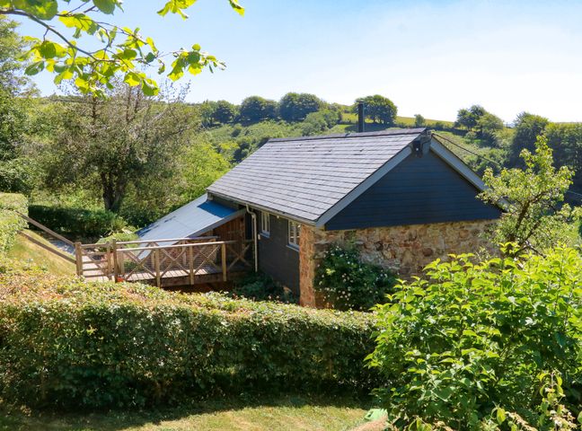 A stone and wood house with a slate roof surrounded by trees and hedges in a rural area at Higher Bumsley Barn in Parracombe