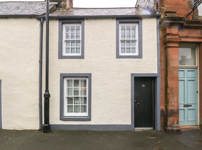 Front exterior of a small two-story building with white walls gray window frames and a black door numbered 51 next to a lamppost at The Precinct House in Whithorn