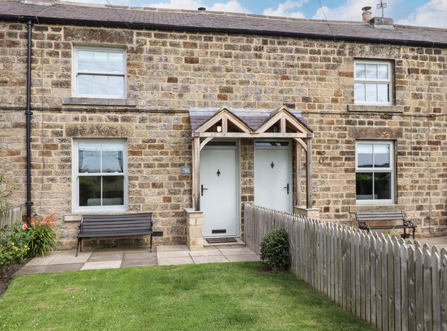 Stone house exterior with two white doors under wooden porch and two benches in front garden at Holida Hoose in Belford
