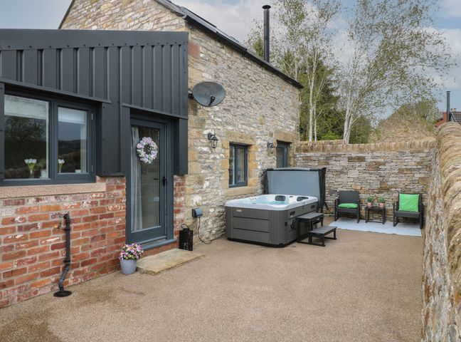 An outdoor patio area with a hot tub and seating against a stone wall at The Bottling Shed in Oker near Matlock