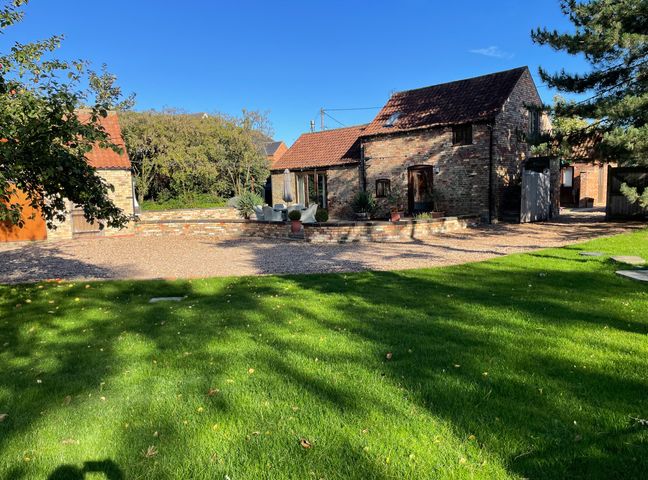 A garden with green grass and trees in front of a brick house with a tiled roof and a gravel driveway at Fair Lea Barn in Stainton By Langworth near Lincoln