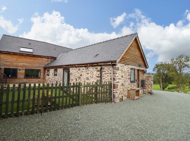 A stone and wood house with a fenced yard and gravel driveway at Y Granar in Llanrhaeadr-Ym-Mochnant