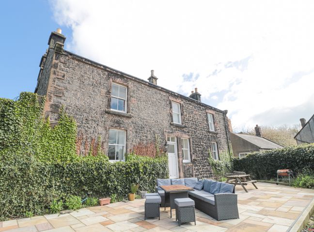 A stone house with ivy on the walls and a patio with outdoor seating and a picnic table at Jubilee House in Embleton