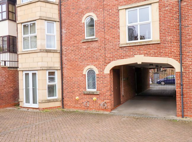 An exterior view of a brick building with an arched entrance leading to a gated parking area at Cadliam in Whitby