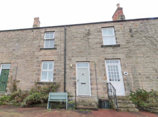 A stone exterior of a terraced house with two white doors and multiple windows at Lavender Cottage in Glanton