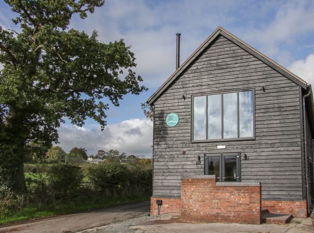 The exterior of a black wooden barn with large windows and a brick wall near a tree at Black Lion Barn Retreat Church Pulverbatch near Pulverbatch