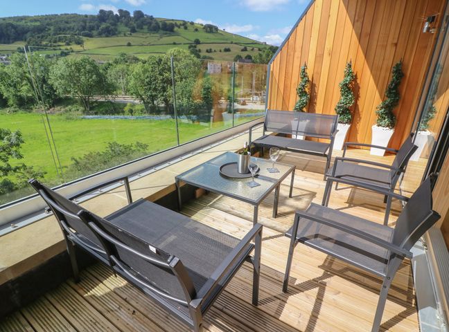 An outdoor balcony with metal chairs a table a bottle of wine and glasses overlooking green hills at The Works in Cononley