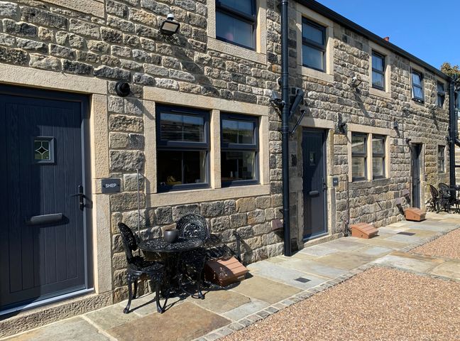 A stone building exterior with black doors and windows and black metal tables and chairs outside Shep Cottage in Cragg Vale
