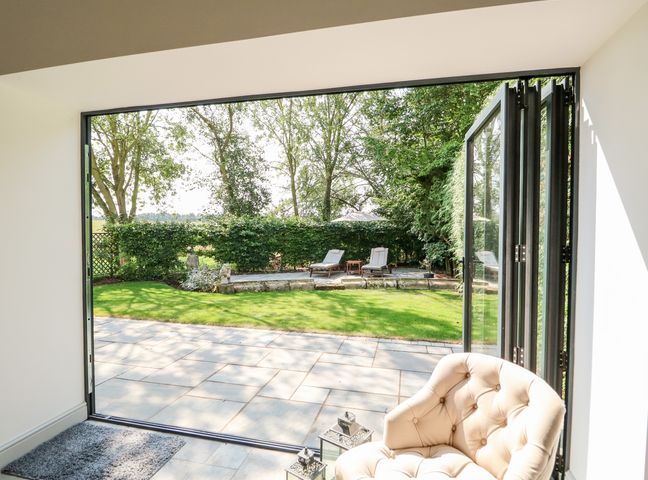 An open folding glass door leading to a garden with two lounge chairs and a small table at The Coach House in Cranwell Village near Lincoln