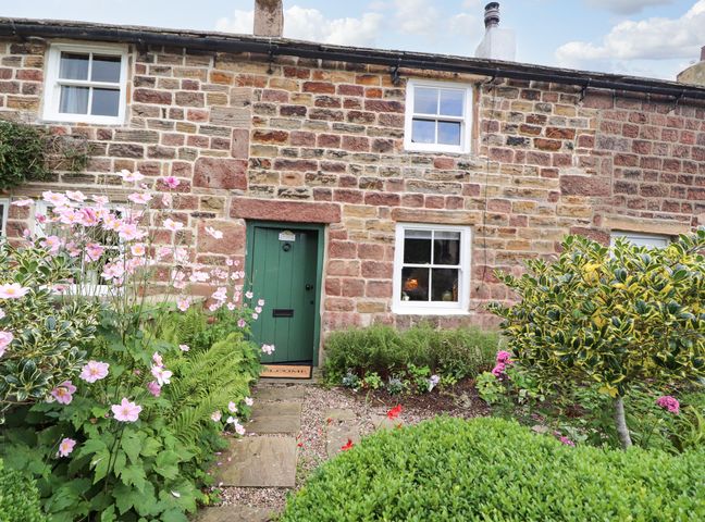 A stone house with a green door and windows surrounded by a garden with plants and flowers at Duckdown in Hurst Green