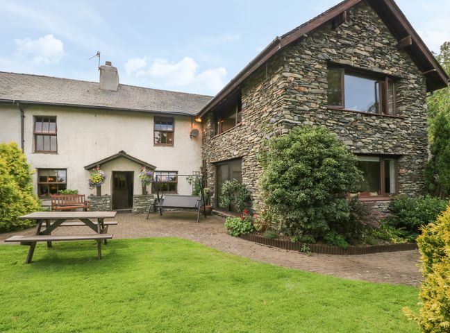 A stone and white cottage with a patio table bench and swing in the garden at 1 Cherry Tree Cottage The Green near Millom Cumbria