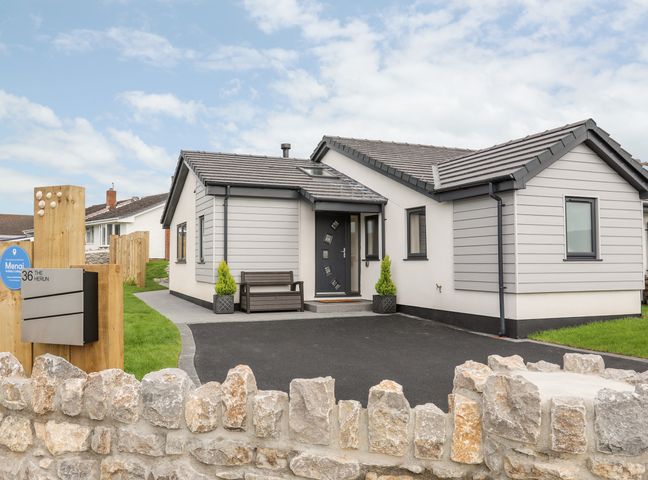 A modern single-story house with a driveway a stone wall and a planted area at The Herun in Rhosneigr