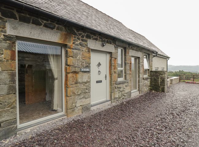 A stone house exterior with windows and a door on a gravel ground at Y Stabl in Llanddoged near Llanrwst