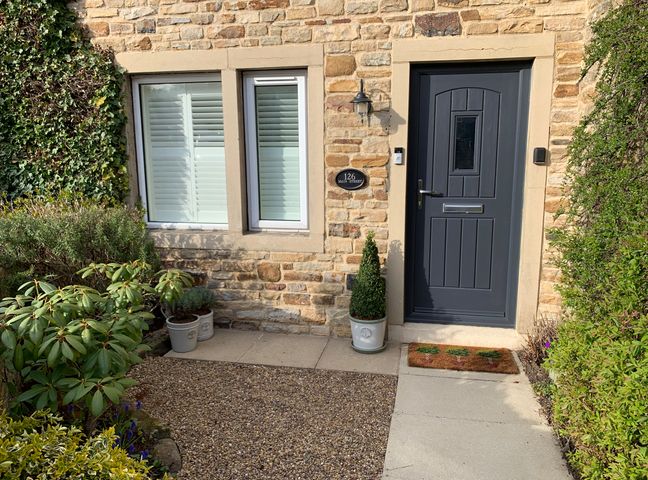 Front door and window of a stone house with potted plants and gravel path at 126 Main Street Cononley