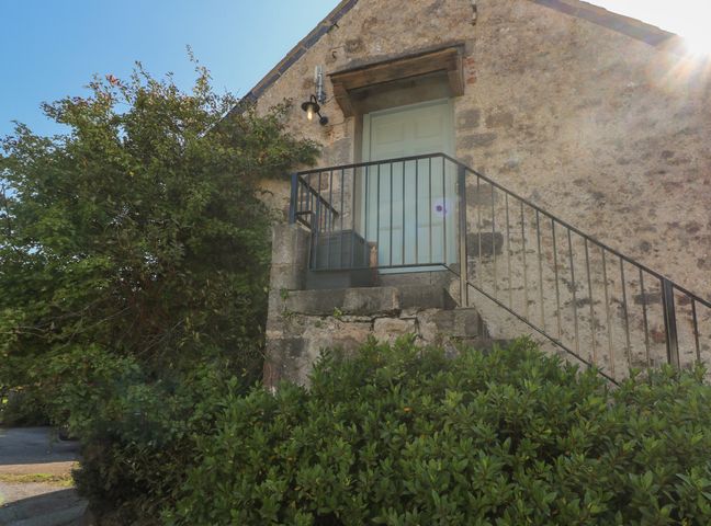 Exterior stone wall with metal railing stairs leading to a pale green door surrounded by greenery at The Coach House in Merrion near Pembroke