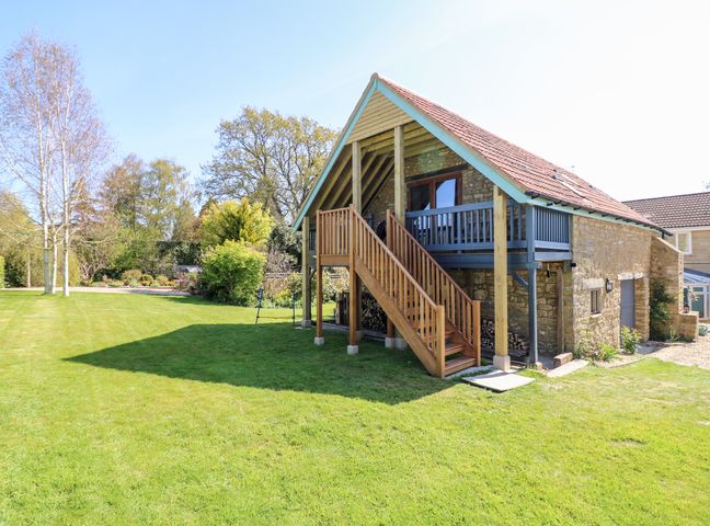 A stone building with wooden stairs leading to a balcony in a garden at Cherrywood Barn in South Petherton