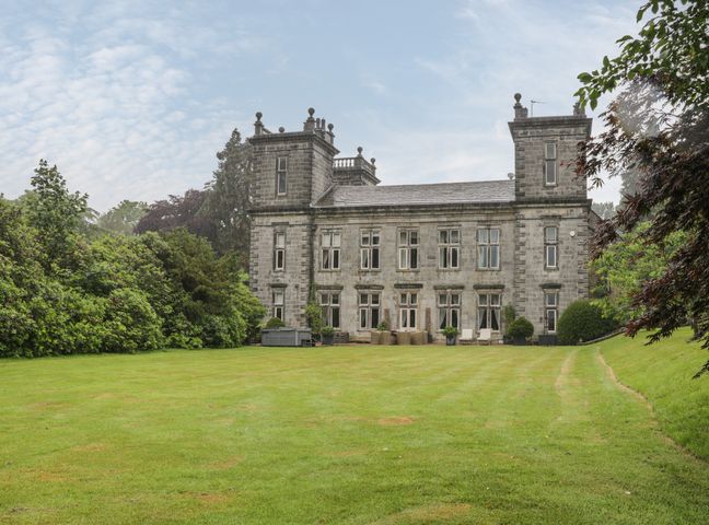 A large stone building with two towers and multiple windows surrounded by lawn and trees at Scale House in Rylstone near Skipton