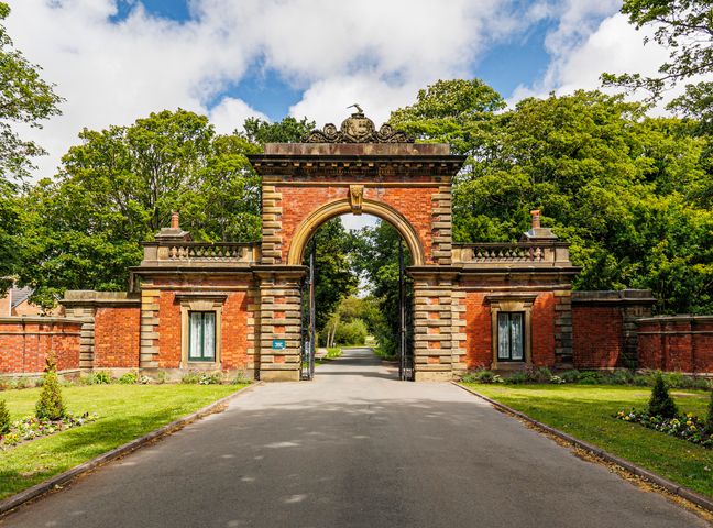 A grand brick and stone archway entrance with iron gates and trees surrounding at Lytham Hall Gate House in Lytham St Annes