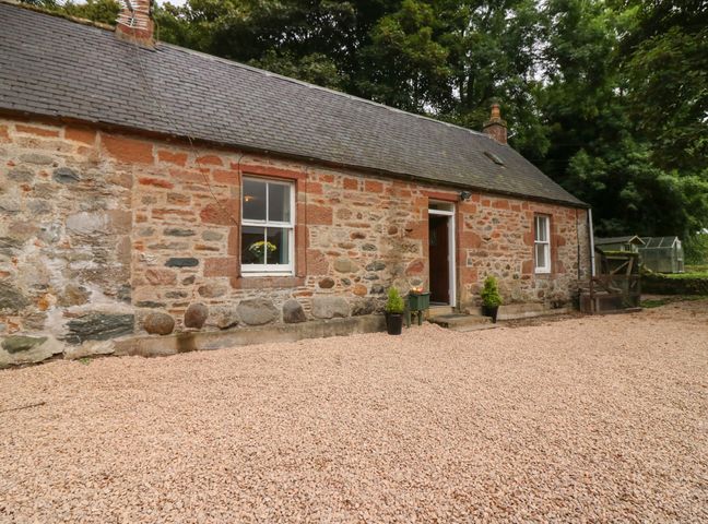 A stone cottage with two windows and a door surrounded by gravel and trees at Gardener's Cottage in Noranside near Kirriemuir