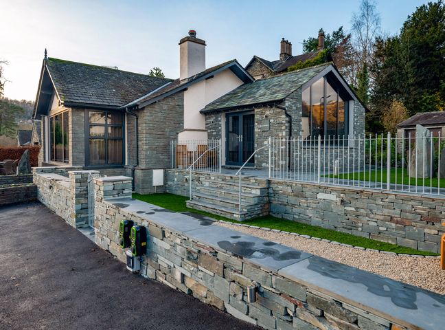 A stone house with large windows and a paved pathway at Landower House in Ambleside